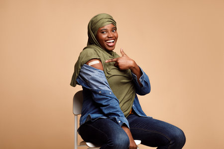 Vaccinated Black Muslim Woman Gesturing Thumbs-Up Approving Vaccination, Beige Backgroundの写真素材
