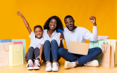 Happy black family with laptop, credit card and shopping bags.の写真素材