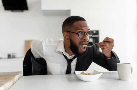 Black man rushing to work eating cereal at homeの写真素材