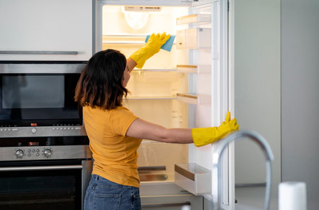 Young Housewife Wiping Shelves In Empty Fridge While Doing Cleaning In Kitchenの写真素材