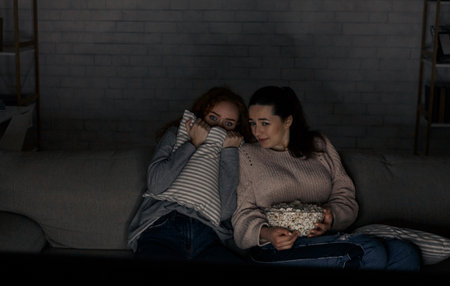 Scared girls watching horror movie on tv sitting on couchの写真素材