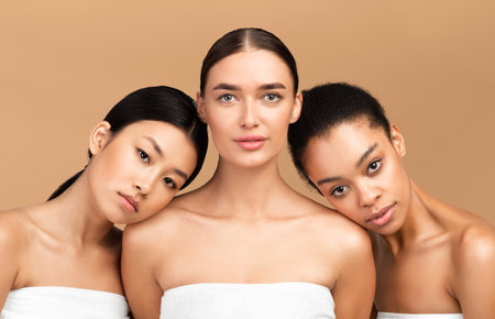 Three Girls Wrapped In Towels Posing Over Beige Backgroundの写真素材