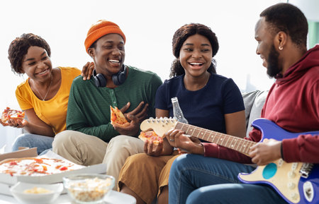 Cute black friends playing guitar and singing together at homeの写真素材
