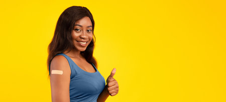 Vaccinated Black Female Showing Thumbs-Up And Arm, Yellow Background, Panorama