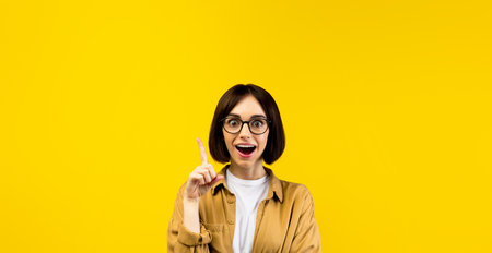 Excited lady having creative idea, raising finger up, yellow background