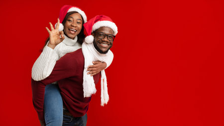 Black Man Carrying Woman Piggyback Wearing Santa Hats, Yellow Backgroundの写真素材