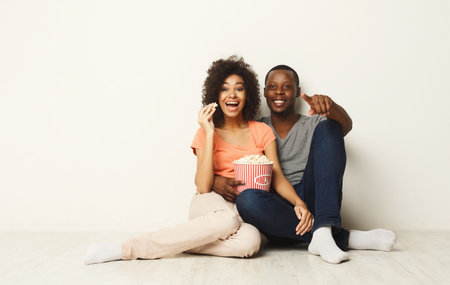 Happy couple enjoying popcorn while sitting on floor at homeの写真素材