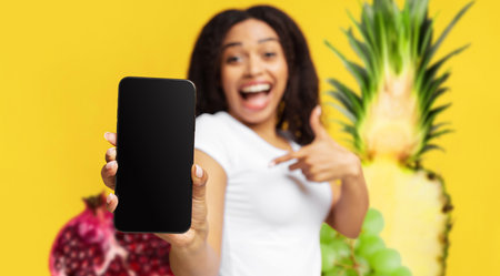Surprised Lady Showing Blank Smartphone Against Bright Yellow Background With Fruits Generative AIの写真素材