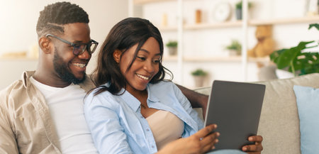 African american couple sitting on couch, using tabletの写真素材