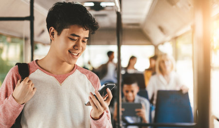 Young Man Smiles While Using His Smartphone on the Bus During the Afternoon Commuteの写真素材
