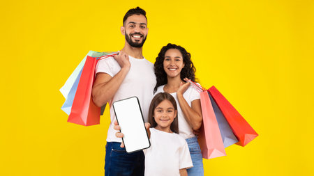 Middle-Eastern Family Showing Smartphone Posing With Shopping Bags, Yellow Backgroundの写真素材