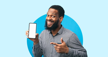 Cheerful Man Holding Smartphone and Pointing at Screen in Bright Blue Backgroundの写真素材