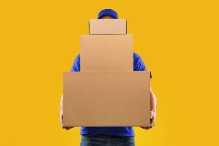 Unrecognizable Courier Holding Many Cardboard Boxes Delivering Packages, Yellow Background