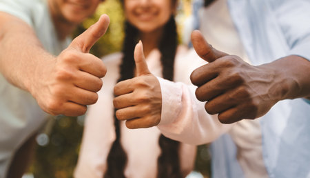 Happy international student friends posing together in park outdoors and showing thumbs up,...