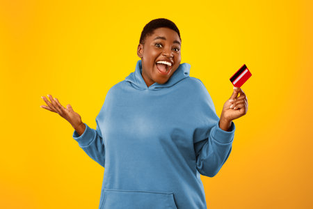 Cheerful Oversized Black Lady Showing Credit Card On Yellow Backgroundの写真素材