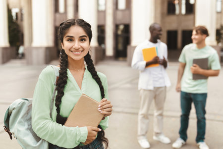 Portrait of happy indian female student posing outdoors in campus with her classmatesの写真素材