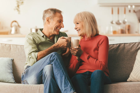 Happy Senior Couple Drinking Coffee Holding Mugs Sitting At Homeの写真素材