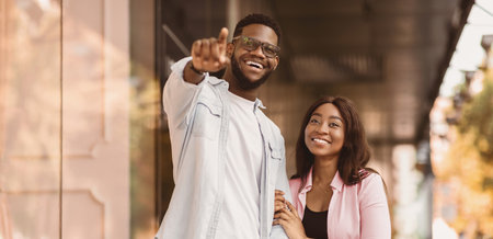 Excited black couple with shopping bags pointing asideの写真素材
