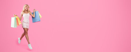 Excited blonde woman jumping with shopping bags at studioの写真素材