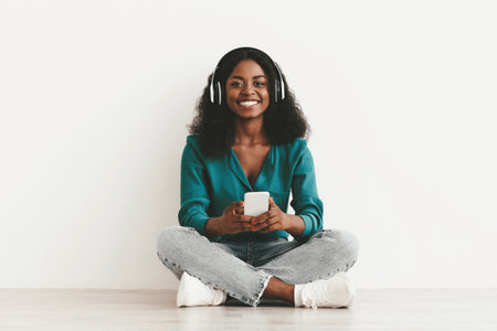 Cheerful black woman using smartphone and wireless headsetの写真素材