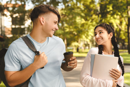Happy multiracial university students walking together in park or in college campus, chatting outdoors during breakの写真素材