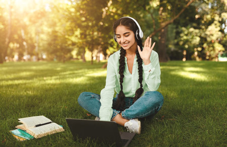 Remote learning. Excited indian female student using laptop, having online lesson and waving to...