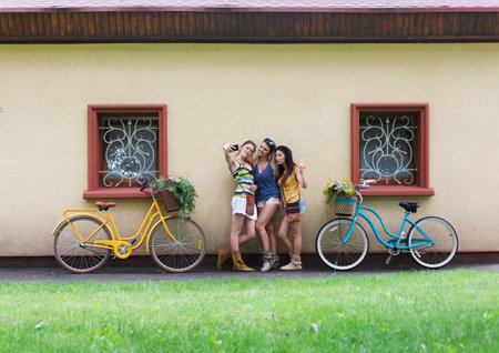 Happy boho chic girls pose with bicycles near house facadeの写真素材