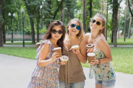 Three beautiful young girls eat donuts in park.