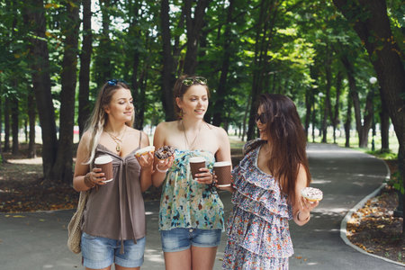 Three beautiful young girls eat donuts in park.の写真素材
