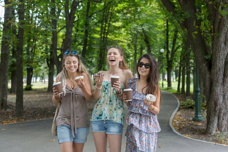 Three beautiful young girls eat donuts in park.の写真素材