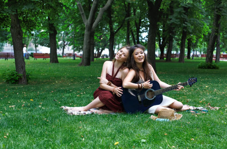 Two happy boho chic stylish girlfriends with guitar, picnicの写真素材