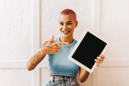 Young Woman With Short Pink Hair Shows Tablet in Bright Room While Smilingの写真素材