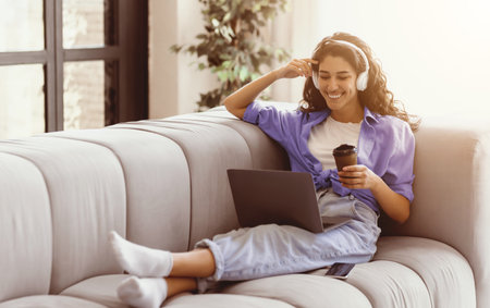 Young Woman Enjoys Relaxing Time While Working on Laptop in Cozy Living Roomの写真素材