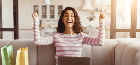 Excited Woman Celebrating Her Online Shopping Success at Homeの写真素材