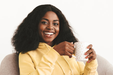 Positive attractive black lady chilling alone at home, drinking coffeeの写真素材