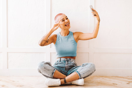 Young Woman With Pink Hair Taking a Selfie While Sitting on the Floor in a Bright Spaceの写真素材