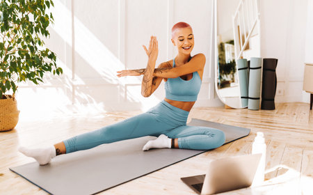 Female Yoga Practitioner Stretching in a Bright Room With a Laptop in the Morningの写真素材