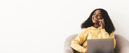 Happy young black woman having phone conversation, using laptopの写真素材