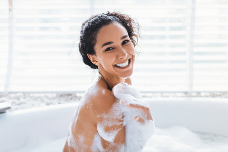 Young Woman Enjoys a Relaxing Bubble Bath With a Joyful Expression in a Bright Bathroomの写真素材