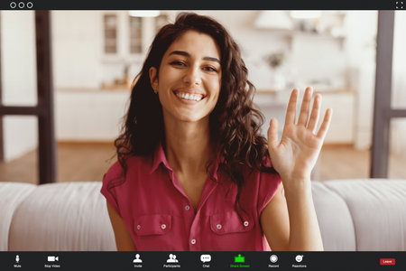 Smiling Young Woman Waves During Online Meeting From Cozy Living Room Settingの写真素材