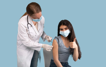 Successful covid-19 vaccination. Teenage girl showing thumb up gesture while being immunized against...