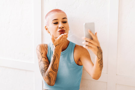 Young Woman With Pink Hair Takes Selfie and Blows Kiss in Modern Indoor Settingの写真素材