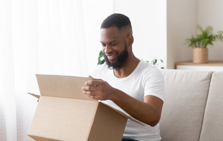 Online shopaholic. Glad african american man unpack parcel