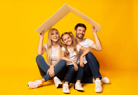 Family Housing. Parents And Daughter Sitting Under Roof, Studio Shotの写真素材