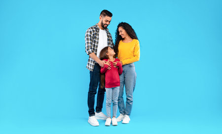 Middle Eastern Parents Embracing Their Happy Daughter On Blue Backgroundの写真素材