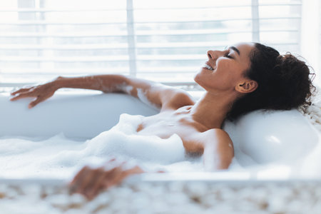 Woman Enjoying a Relaxing Bubble Bath in a Beautiful, Bright Bathroom Settingの写真素材