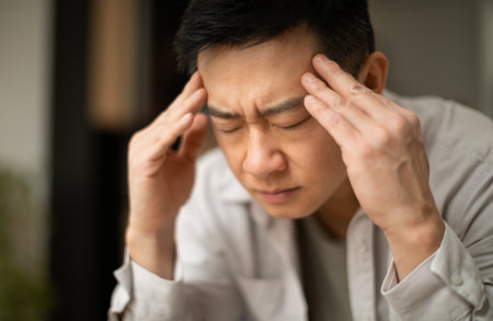 Closeup of asian middle aged man suffering from headache, touching his temples, sitting with closed eyes, copy spaceの写真素材