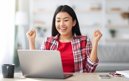 Joyful Excited Asian Lady Celebrating Success With Laptop At Homeの写真素材