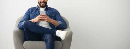 Man Using Smartphone While Sitting Comfortably in an Armchair at Homeの写真素材