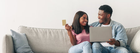 Black couple using pc and credit card at homeの写真素材